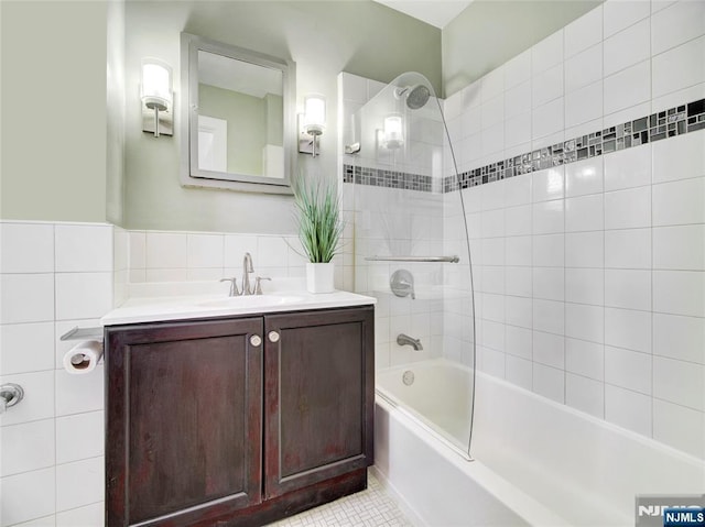 bathroom with tile walls, tile patterned flooring, tiled shower / bath combo, and vanity