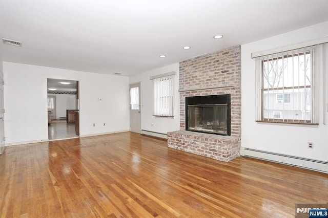 unfurnished living room featuring wood-type flooring, a brick fireplace, and baseboard heating