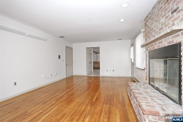 unfurnished living room featuring a baseboard radiator, a fireplace, and light wood-type flooring