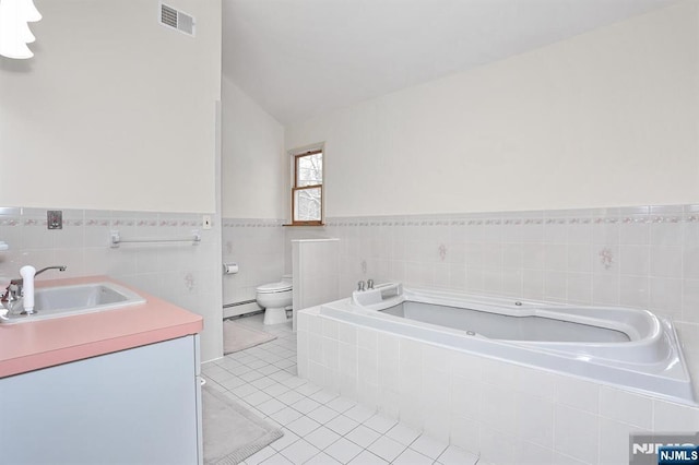 bathroom with tiled tub, baseboard heating, tile patterned flooring, vanity, and toilet