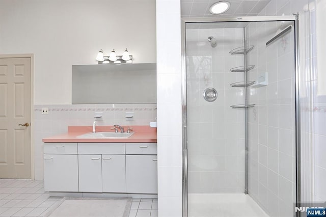 bathroom featuring tile patterned flooring, vanity, tile walls, and a shower with shower door