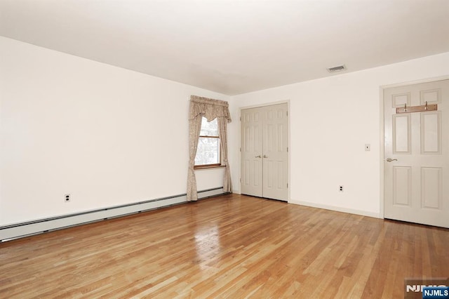 empty room with light hardwood / wood-style floors and baseboard heating