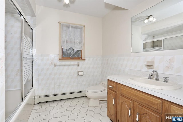 full bathroom featuring toilet, tile walls, baseboard heating, vanity, and enclosed tub / shower combo