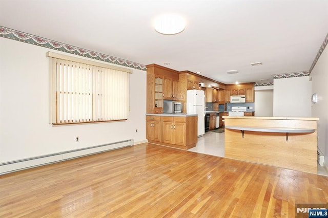 kitchen with a kitchen bar, baseboard heating, kitchen peninsula, white appliances, and light hardwood / wood-style flooring