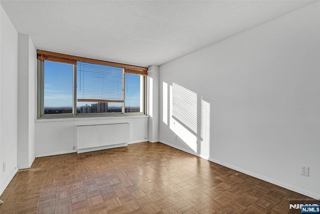 spare room with radiator, baseboards, and a textured ceiling