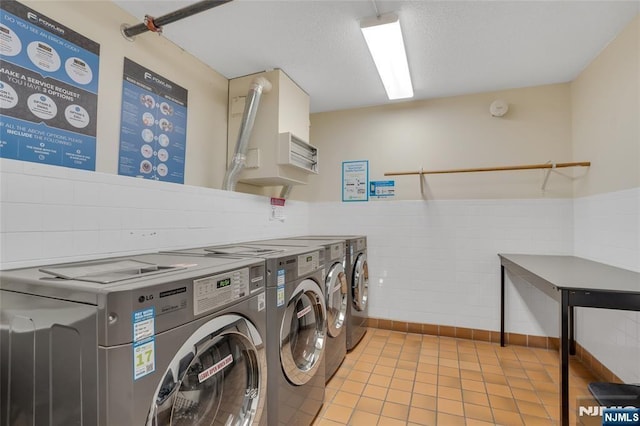 common laundry area with a wainscoted wall, tile walls, light tile patterned flooring, a textured ceiling, and separate washer and dryer