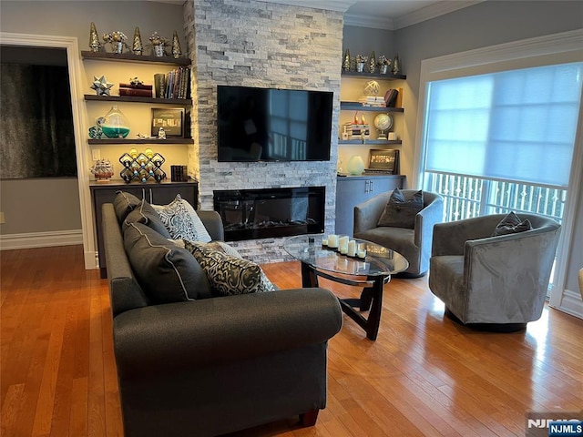 living room featuring built in features, wood-type flooring, a stone fireplace, and ornamental molding