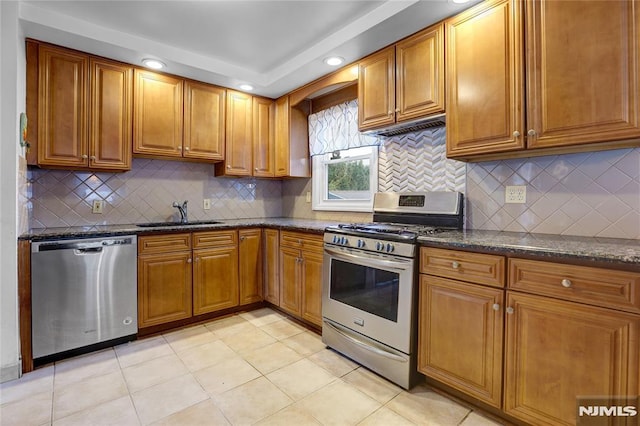 kitchen featuring sink, tasteful backsplash, light tile patterned floors, dark stone countertops, and appliances with stainless steel finishes