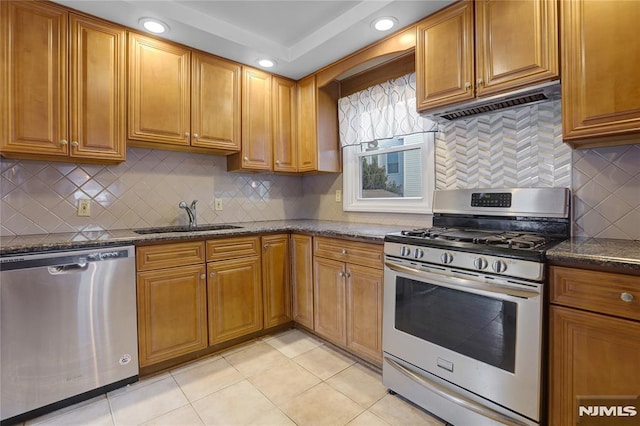 kitchen with sink, ventilation hood, light tile patterned floors, dark stone countertops, and appliances with stainless steel finishes