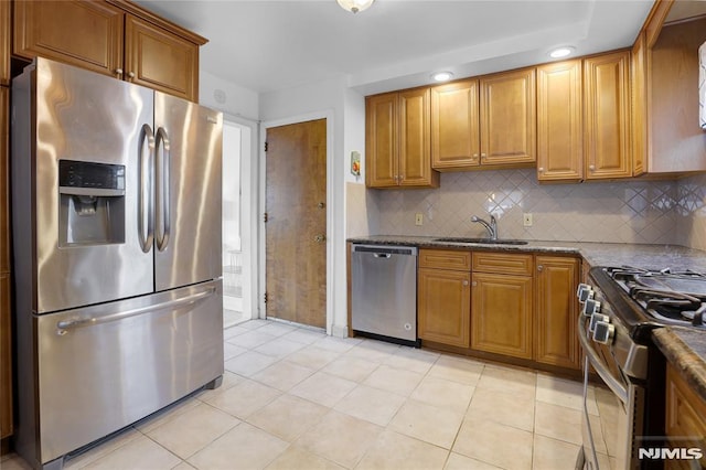 kitchen featuring sink, light tile patterned floors, dark stone counters, stainless steel appliances, and decorative backsplash