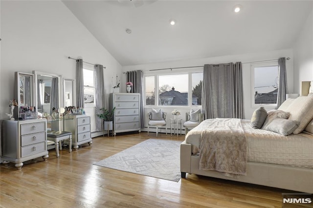 bedroom with a baseboard heating unit, high vaulted ceiling, multiple windows, and light wood-type flooring