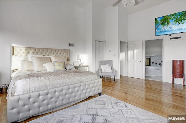 bedroom with a high ceiling, wood-type flooring, and ensuite bath