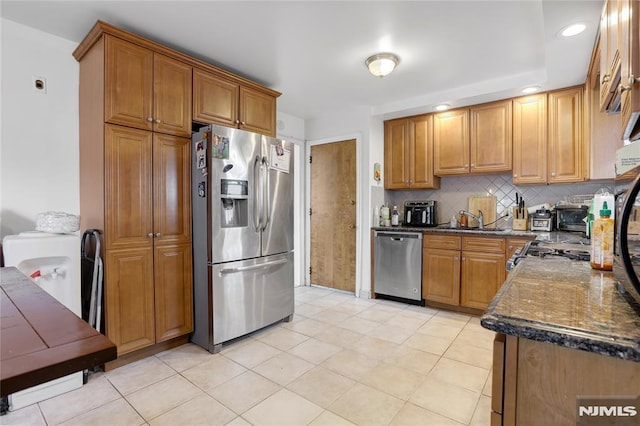 kitchen featuring light tile patterned flooring, sink, appliances with stainless steel finishes, dark stone counters, and backsplash