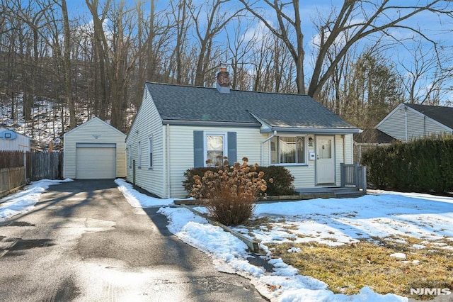 view of front of house with an outbuilding, fence, a chimney, a shingled roof, and aphalt driveway