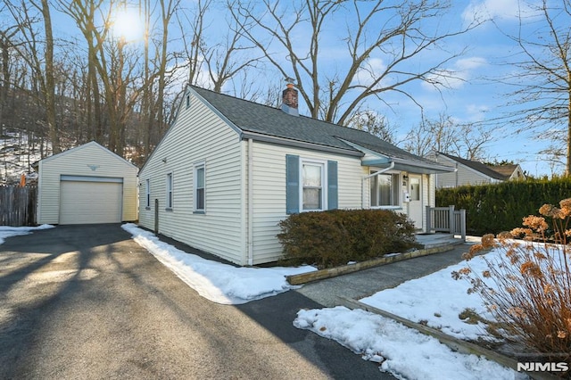 view of front of house featuring driveway, a detached garage, an outdoor structure, a shingled roof, and a chimney