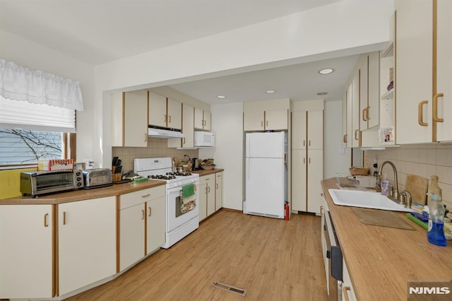 kitchen with white appliances, visible vents, a sink, under cabinet range hood, and light wood-type flooring