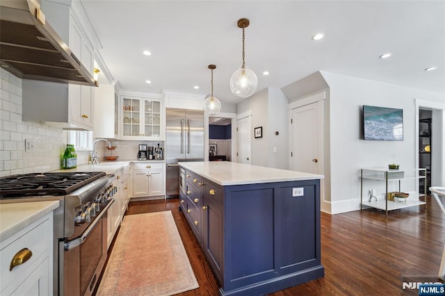 kitchen with white cabinets, wall chimney range hood, premium appliances, decorative light fixtures, and a kitchen island