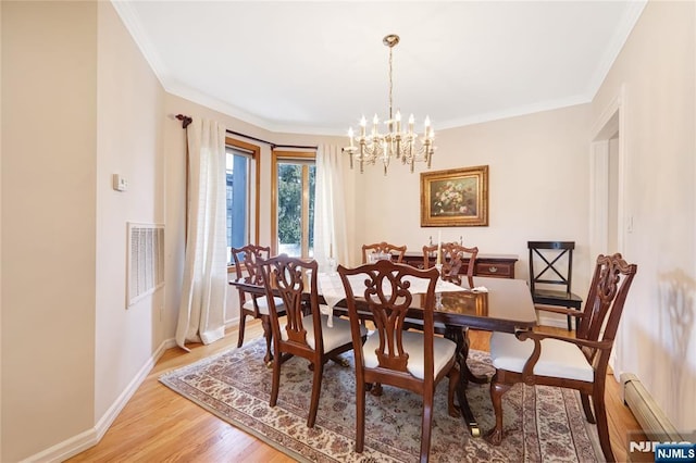 dining area with crown molding, an inviting chandelier, light hardwood / wood-style flooring, and a baseboard heating unit