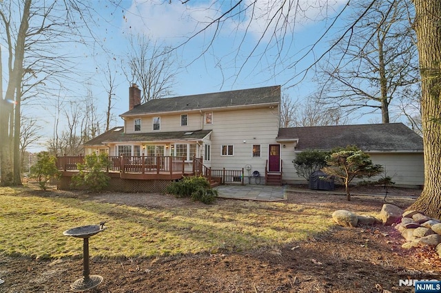 rear view of property featuring a wooden deck, a yard, a chimney, and a patio area