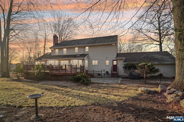 back of house with a shingled roof, a wooden deck, a chimney, a yard, and a patio area