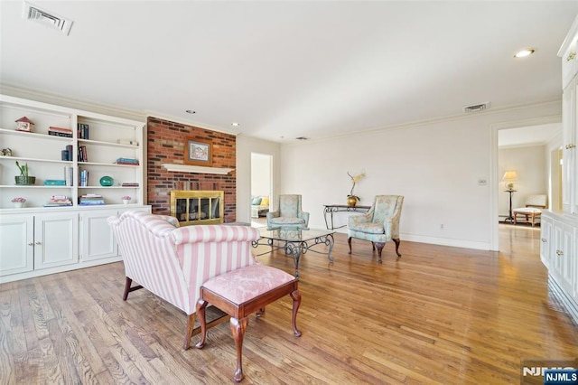 living room featuring visible vents, light wood-style flooring, a fireplace, and ornamental molding