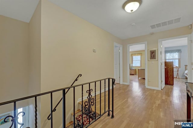 hall featuring baseboards, visible vents, light wood-style flooring, and an upstairs landing