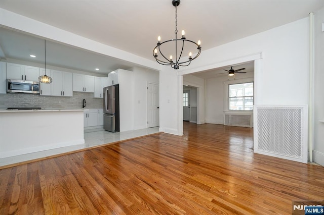 kitchen featuring stainless steel appliances, hanging light fixtures, white cabinets, and light hardwood / wood-style flooring