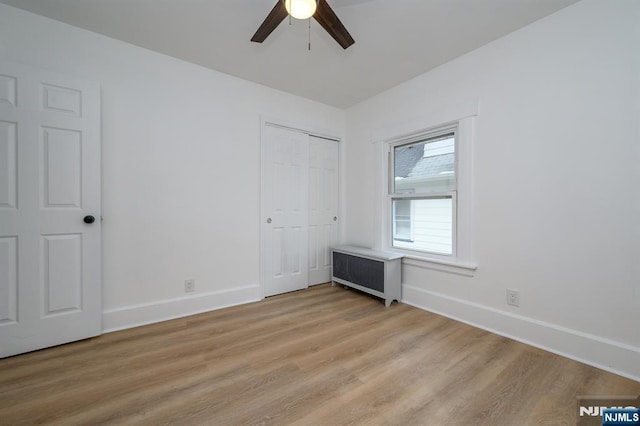 unfurnished bedroom with ceiling fan, radiator, a closet, and light wood-type flooring