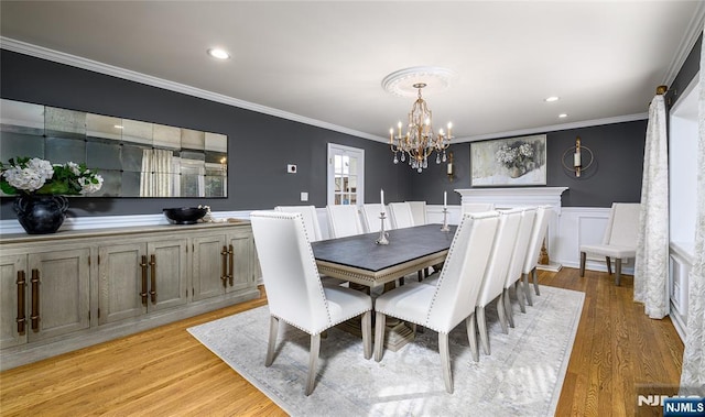 dining space with ornamental molding, light wood-type flooring, a wainscoted wall, and a notable chandelier