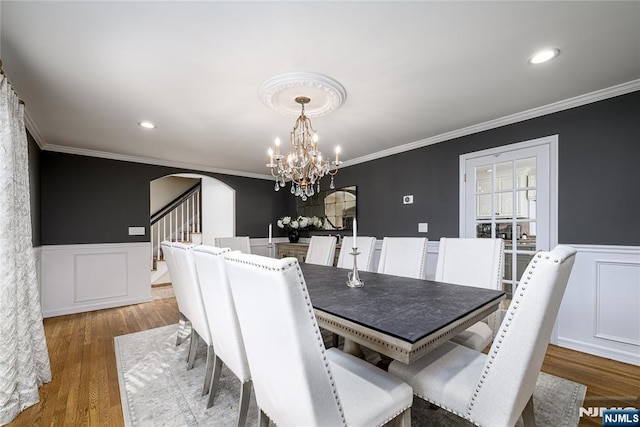 dining room featuring arched walkways, a wainscoted wall, dark wood finished floors, and crown molding