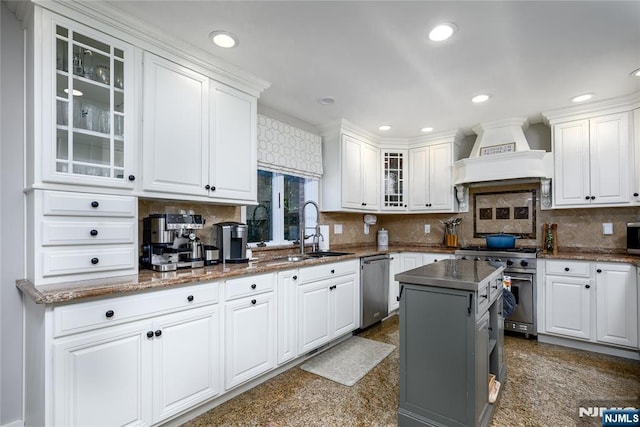 kitchen with dark countertops, glass insert cabinets, appliances with stainless steel finishes, white cabinetry, and premium range hood