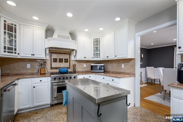 kitchen featuring stainless steel appliances, a kitchen island, white cabinets, custom exhaust hood, and glass insert cabinets