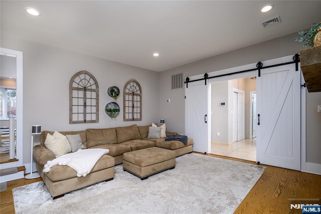 living room featuring a barn door, wood finished floors, visible vents, and recessed lighting