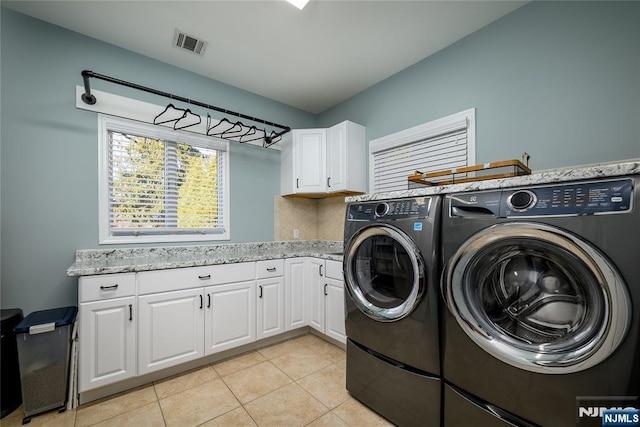 laundry area featuring visible vents, light tile patterned floors, washer and clothes dryer, and cabinet space