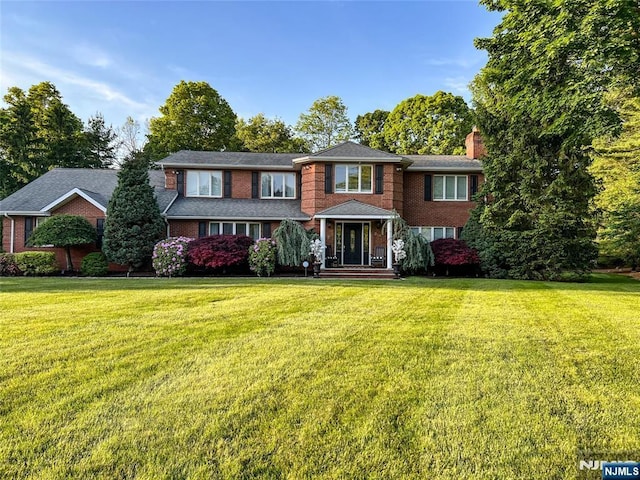 view of front facade with brick siding, a chimney, and a front lawn