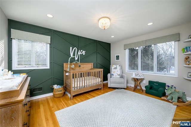 bedroom with light wood finished floors, recessed lighting, visible vents, a decorative wall, and baseboards