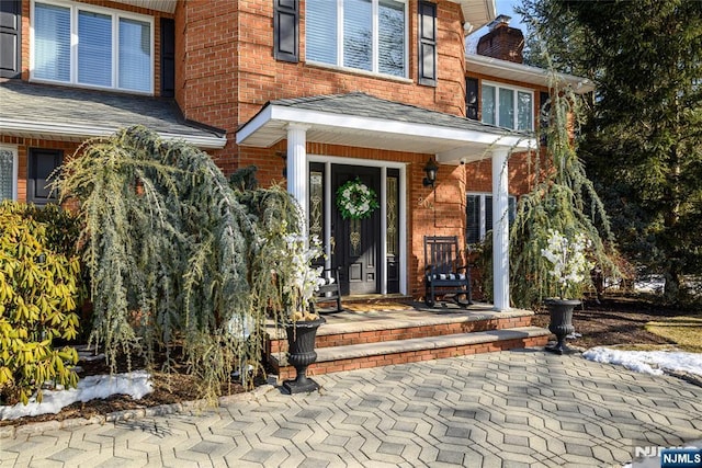 property entrance featuring brick siding, a chimney, and roof with shingles