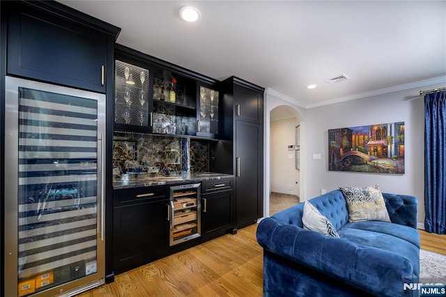 bar with arched walkways, a bar, wine cooler, and light wood finished floors