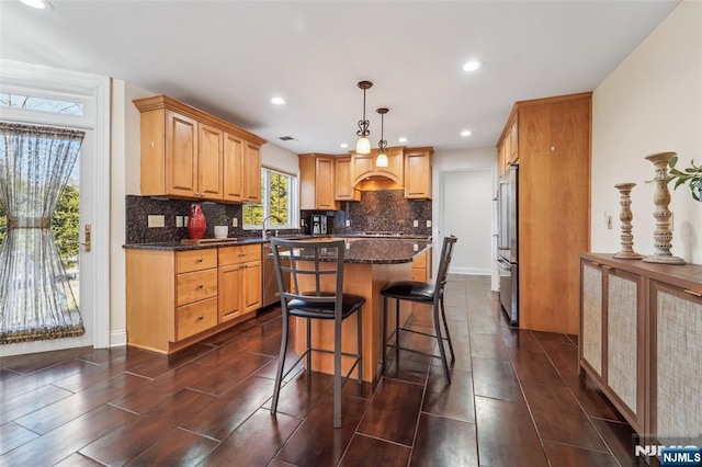 kitchen with a kitchen island, appliances with stainless steel finishes, a breakfast bar, wood finish floors, and backsplash