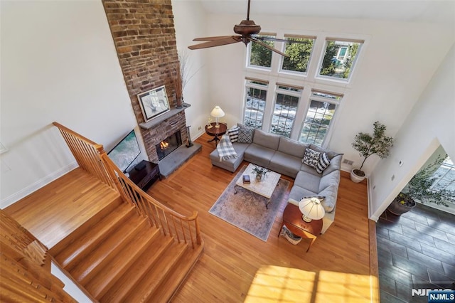 living room featuring a high ceiling, a fireplace, wood finished floors, a ceiling fan, and baseboards