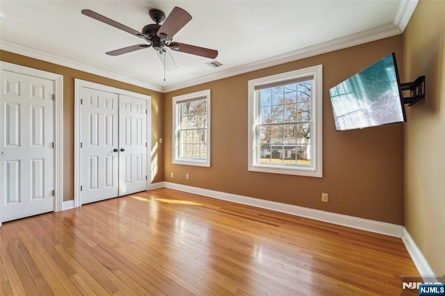 unfurnished bedroom featuring baseboards, light wood-style flooring, visible vents, and crown molding