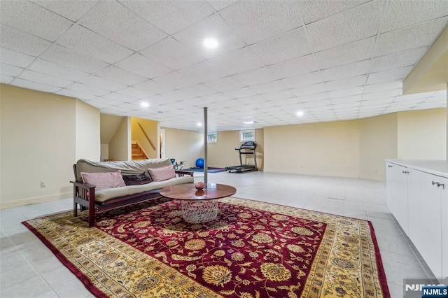 living room featuring a drop ceiling, stairway, baseboards, and light tile patterned floors