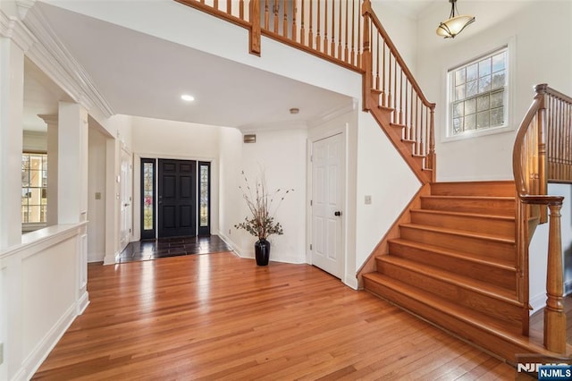 foyer entrance featuring a healthy amount of sunlight, light wood-style floors, stairway, and crown molding