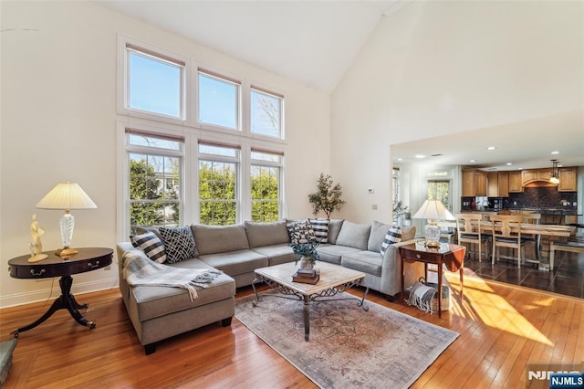 living area with high vaulted ceiling, hardwood / wood-style floors, and baseboards