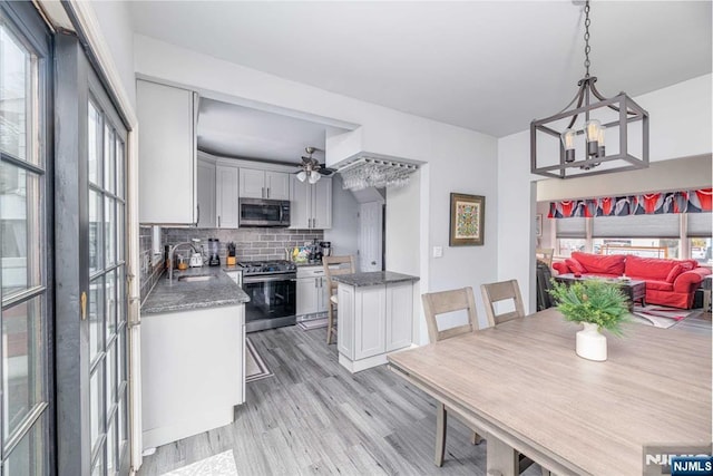 kitchen featuring decorative light fixtures, sink, backsplash, stainless steel appliances, and light hardwood / wood-style flooring