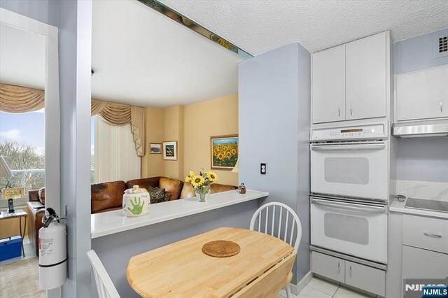 kitchen with a textured ceiling, white cabinets, and double oven