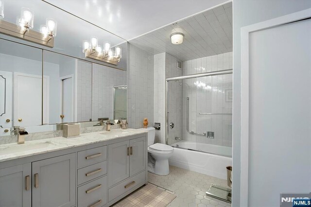 full bathroom featuring toilet, tile patterned floors, bath / shower combo with glass door, and vanity