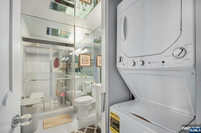 bathroom featuring stacked washer / dryer, tile patterned flooring, and toilet