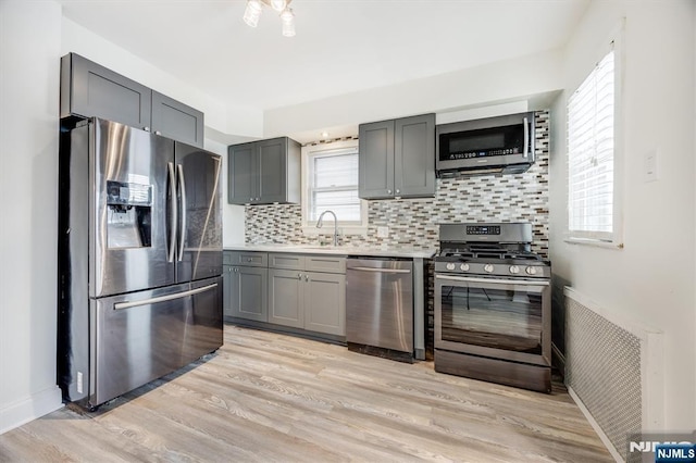 kitchen with appliances with stainless steel finishes, gray cabinets, sink, and light wood-type flooring