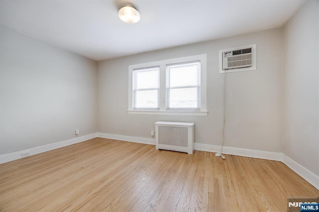 unfurnished room with a wall mounted air conditioner, light hardwood / wood-style flooring, and radiator heating unit